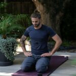 a man sitting on a yoga mat with his hands in his pockets